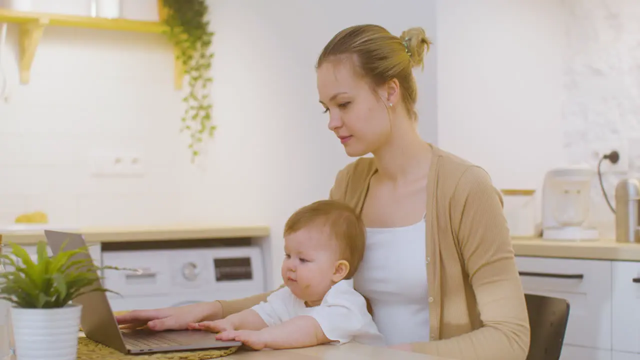 Young Woman Working On Laptop Computer While Sitting With Baby Boy At Home 3