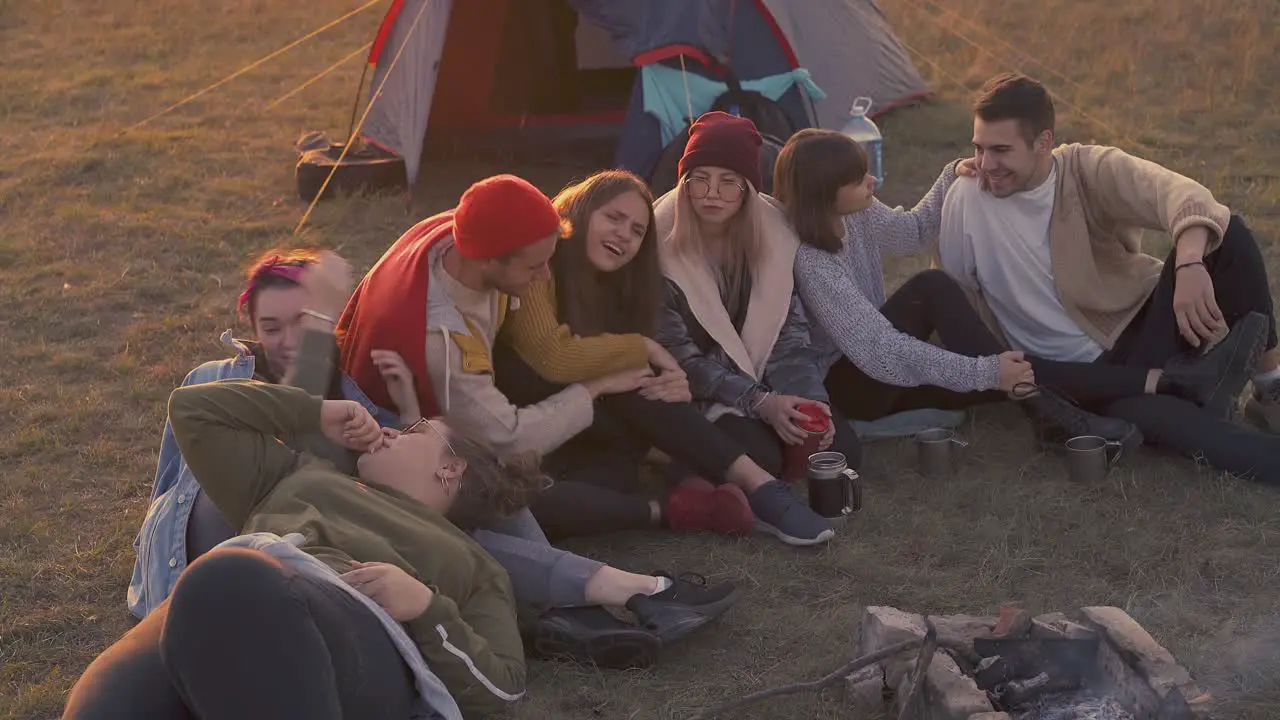 positive tourists rest at burning bonfire in camp in evening