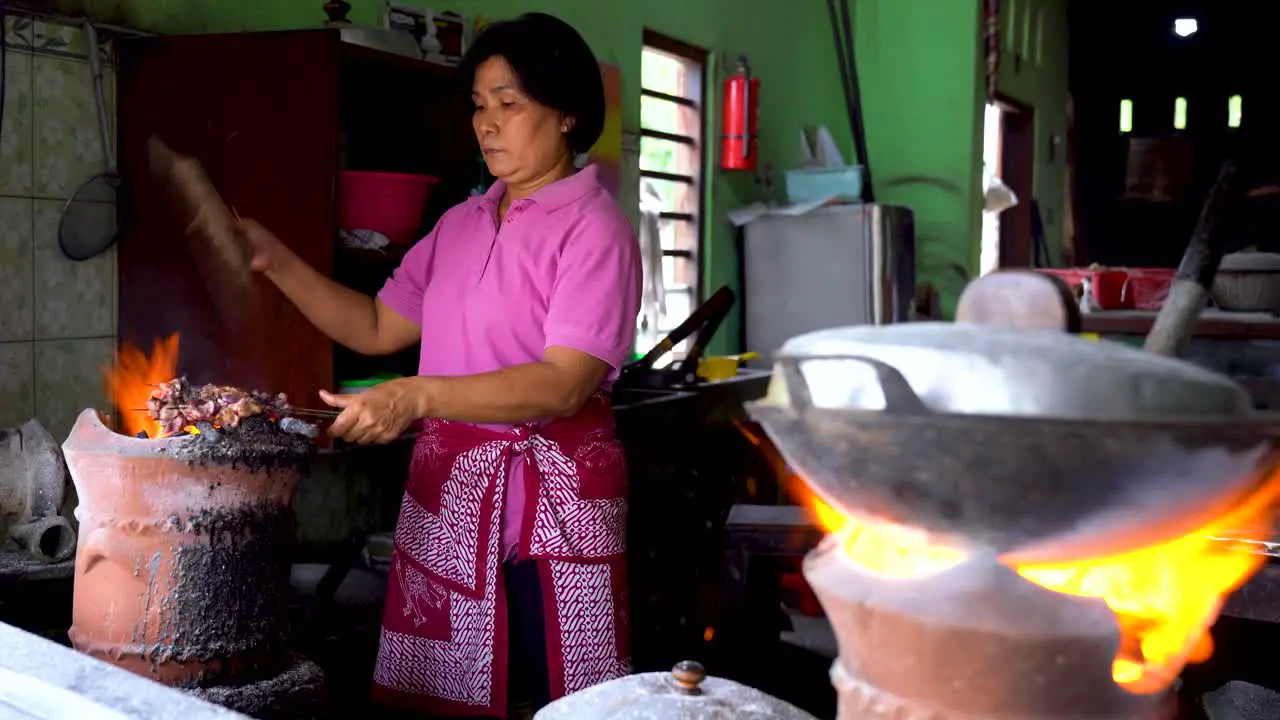 Female chef roasting goat satay on charcoal stove traditional Indonesian dish