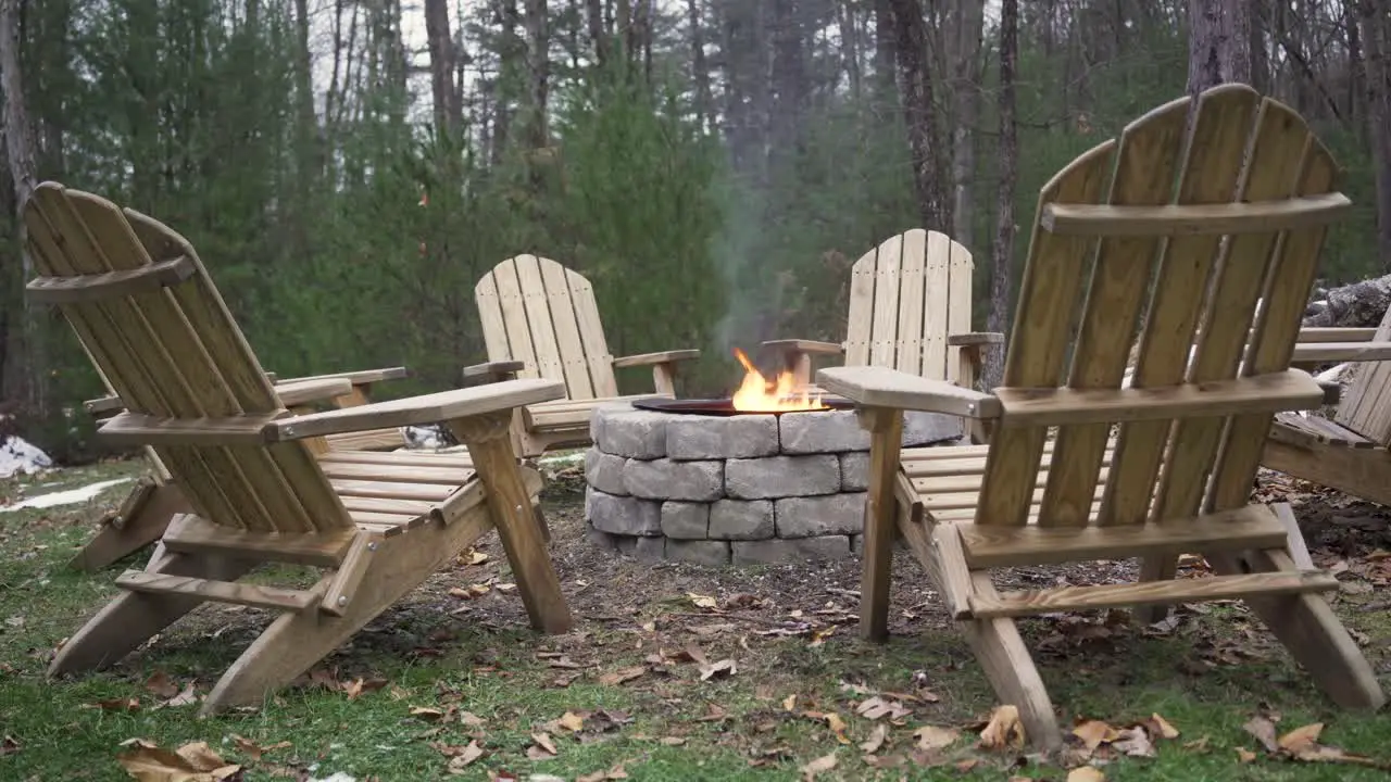 Close up of 6 empty lawn chairs around a burning fire pit