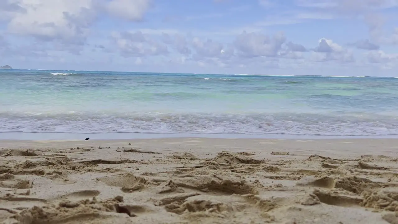 A wide shot of the crystal clear blue water hit shore with sand footprints