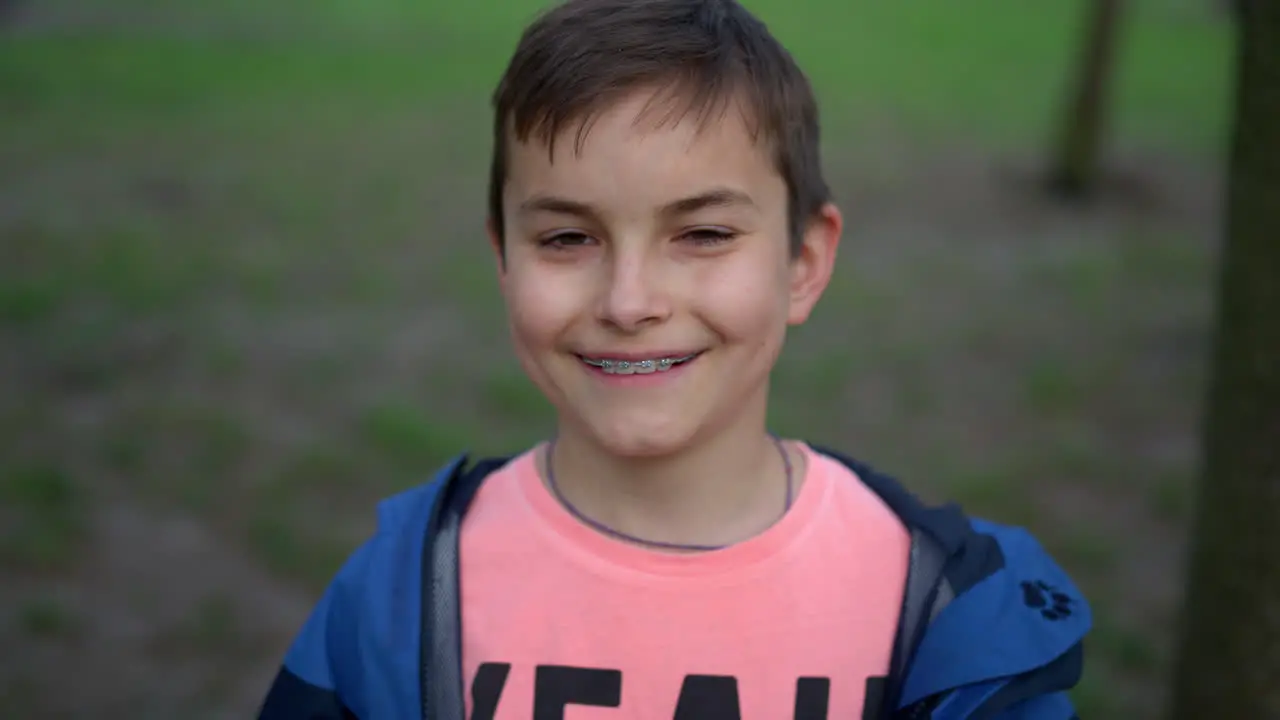 Happy teen boy in brackets looking camera outdoors Handsome guy smiling in park