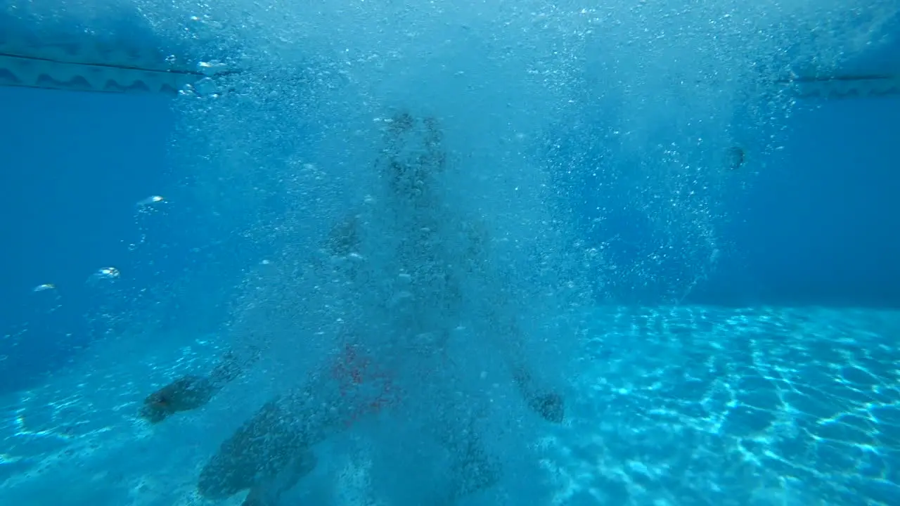 Man with orange swimming shorts jumps into swimming pool in slow motion