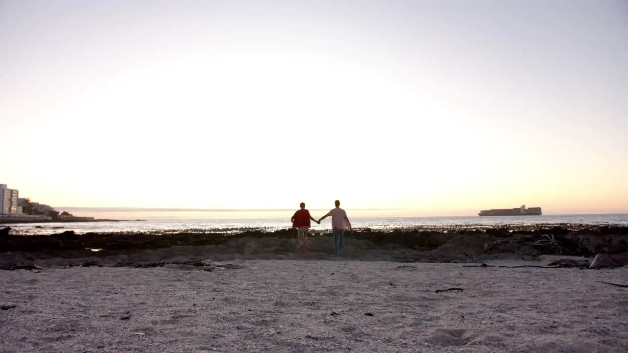 Happy diverse gay male couple running and holding hands at beach slow motion