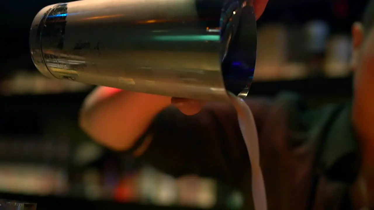 Asian bartender using stainless steel cocktail shaking cup to pour freshly mixed tropical cocktail into glass filmed as close up in slow motion