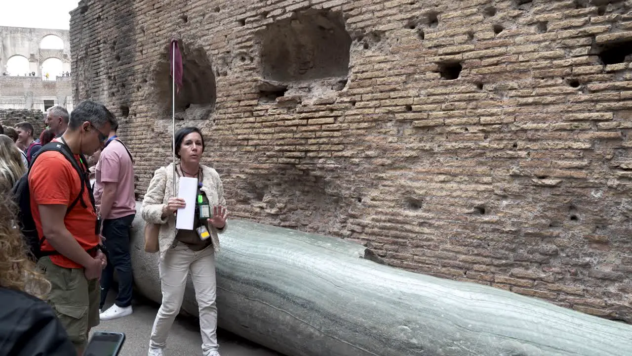 Female Tour Guide Explaining To Tourists About Marble Column Inside The Colosseum In Rome