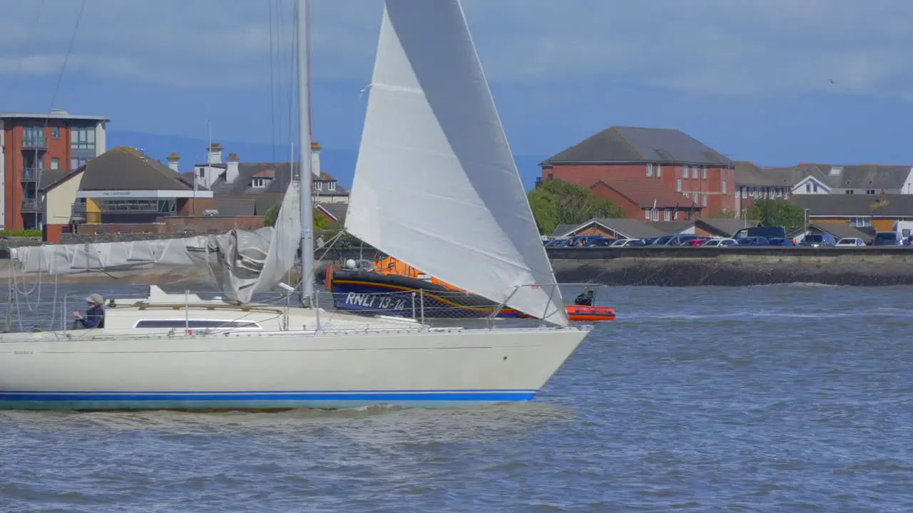 Yacht passing lifeboat on river as lifeboat crew start to disembark