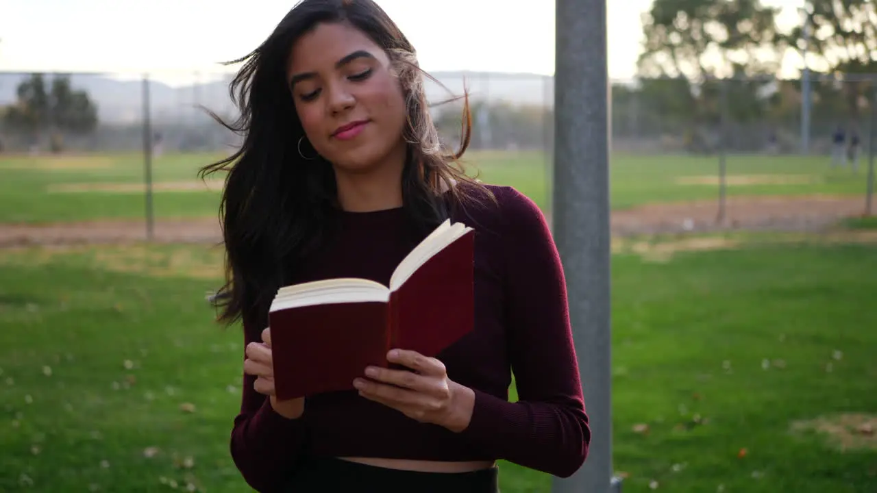 A young woman university student reading a textbook outdoors in the campus park at sunset SLOW MOTION