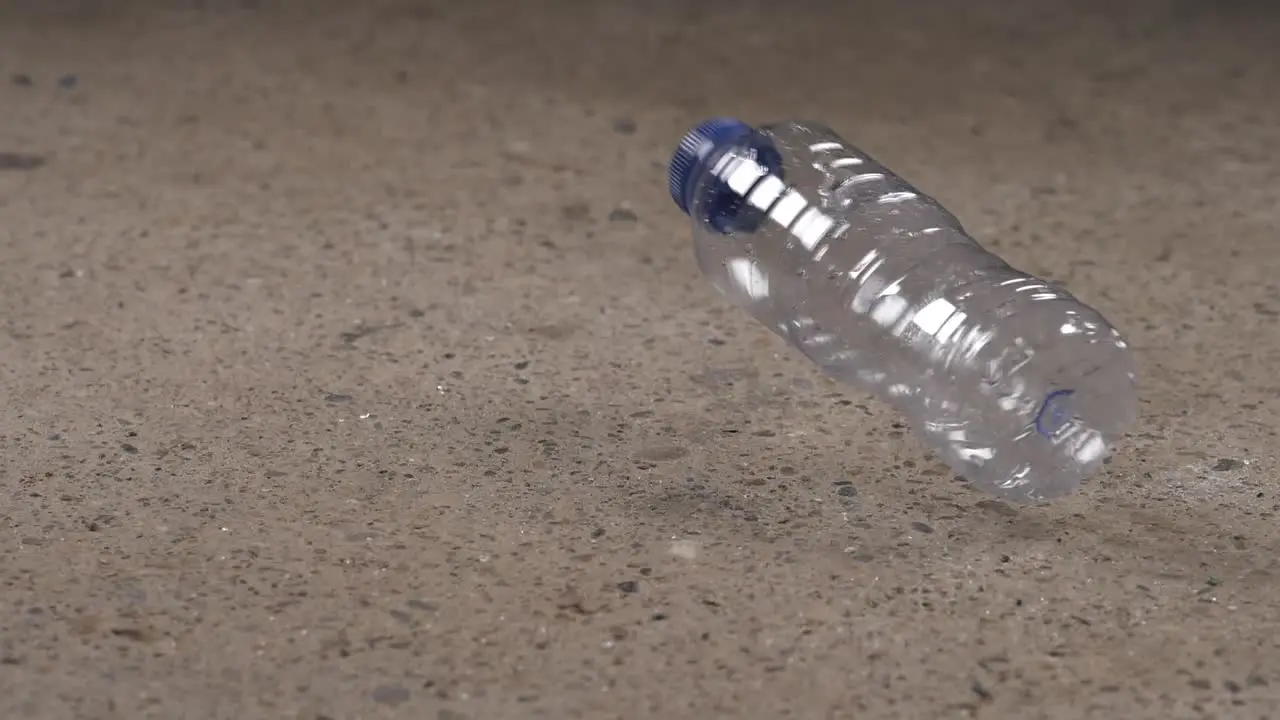 Hammer hits plastic water bottle which bounces and rolls away in slow motion