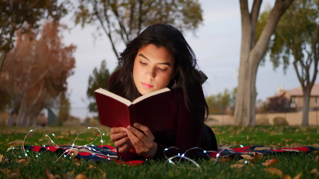 A young adult woman reading a book and using her imagination to bring the story to life outdoors in the park at sunset