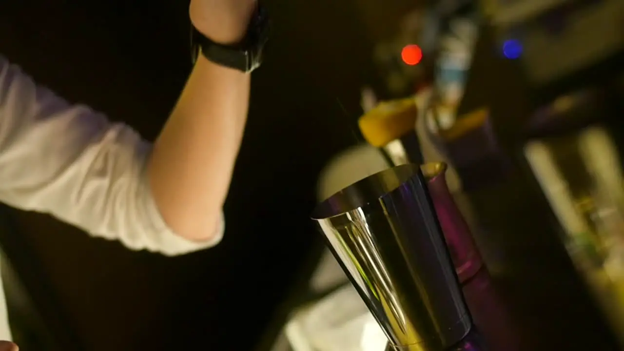 Cocktail mix being poured from bartenders shot measuring cup into stainless steel mixing cup filmed as slow motion close up