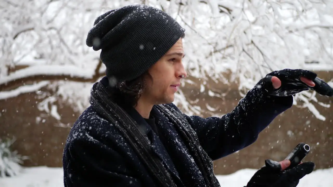 A caucasian man in warm winter clothing looking at his phone in a cold weather snow storm SLOW MOTION