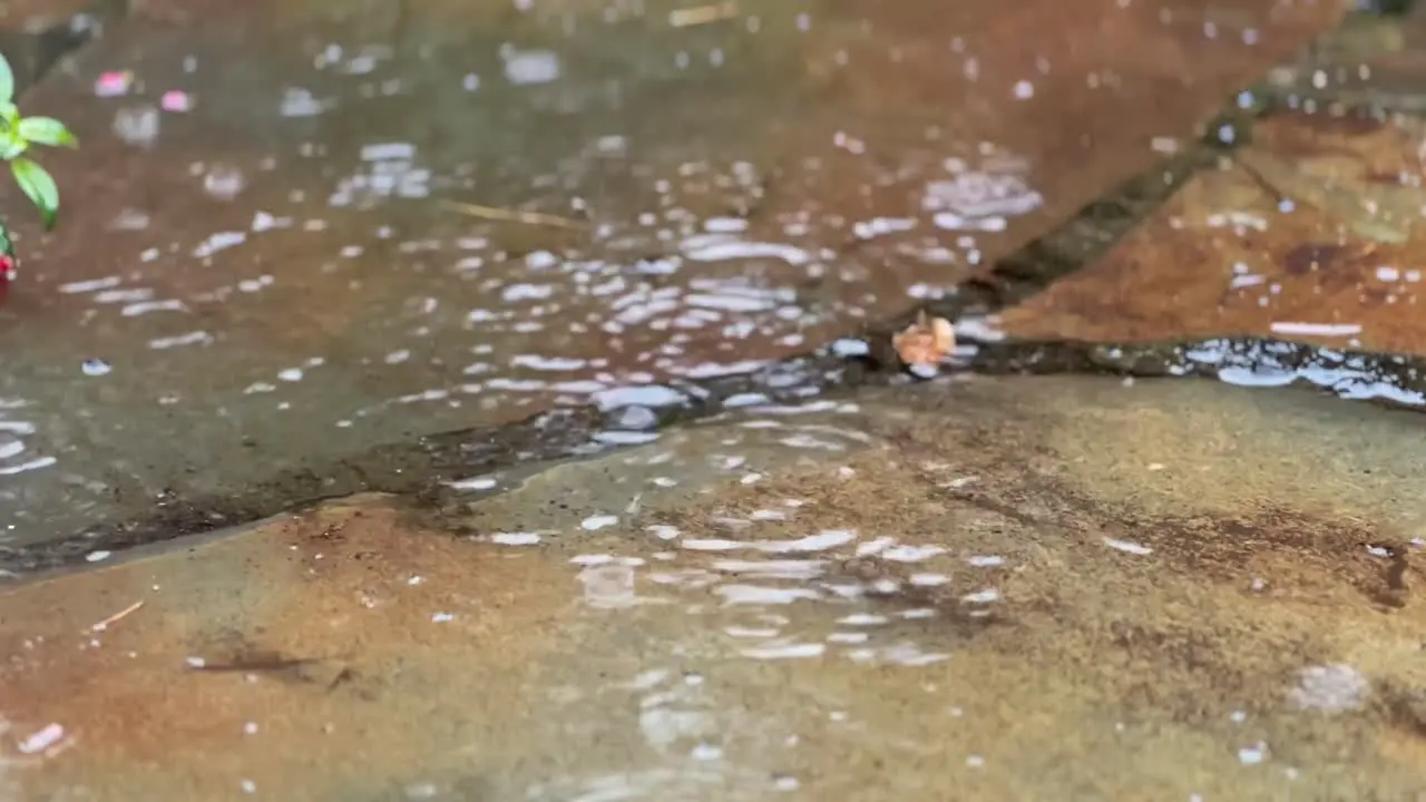 close up of rain water drops falling into big puddle on stones flooding the street climate change concept