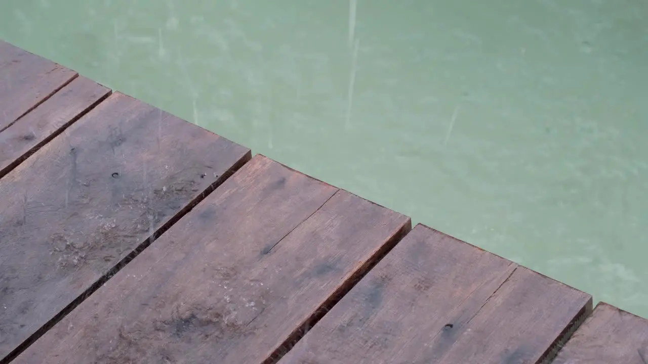 Close up of wooden planks of wharf pier with a glimpse of ocean water and raindrops falling during bad weather storm and raining downpour in tropical destination