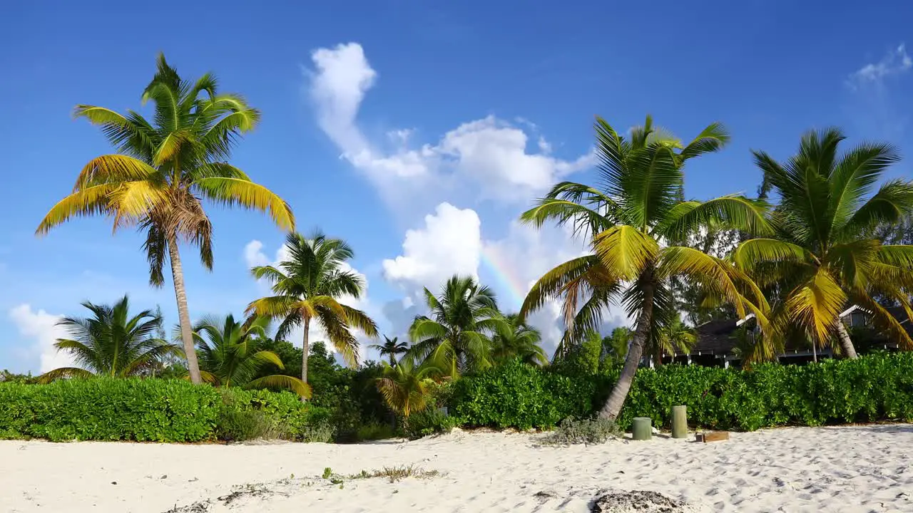 Static video of a tropical beach scene in Exuma Bahamas with a small rainbow in the clouds