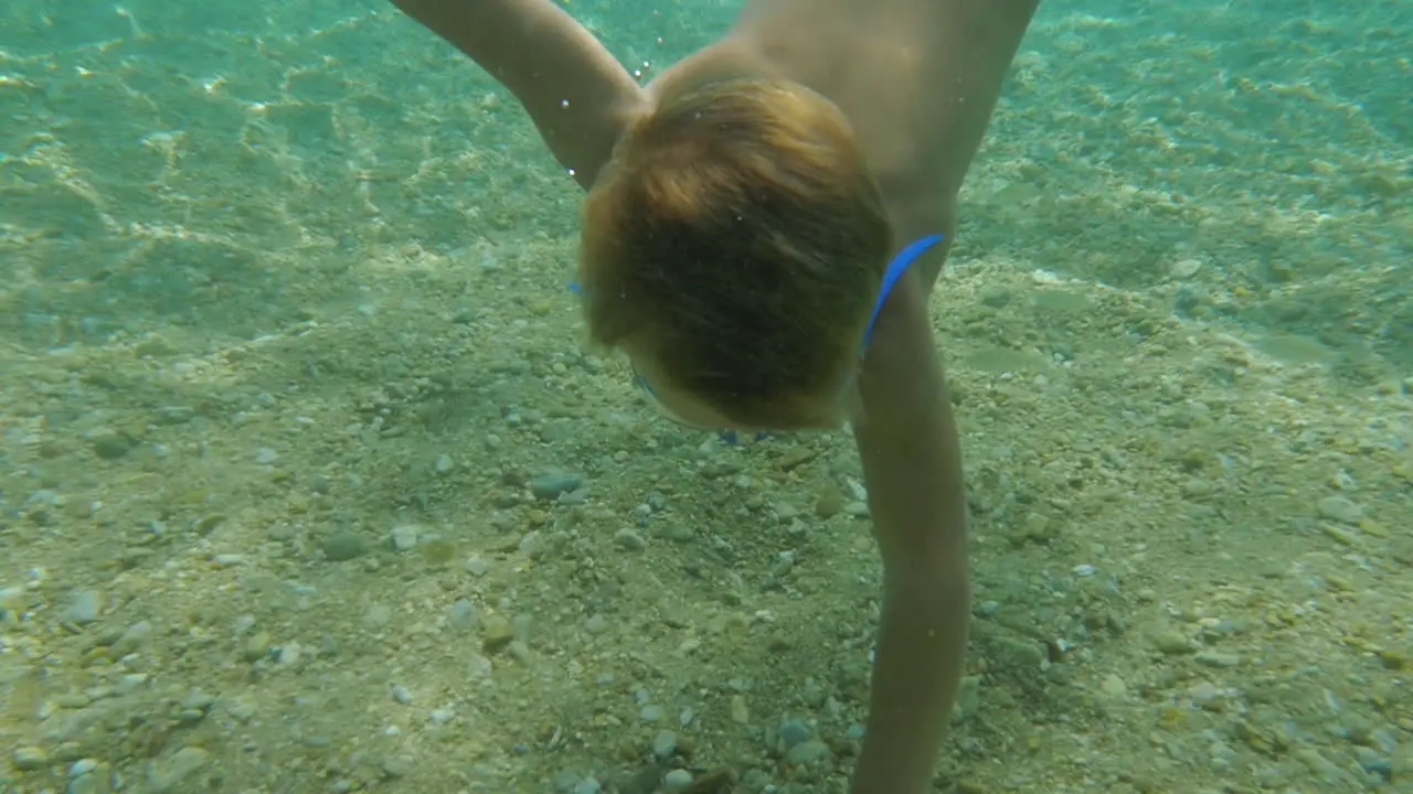 Little boy swimming under the water to take a shell