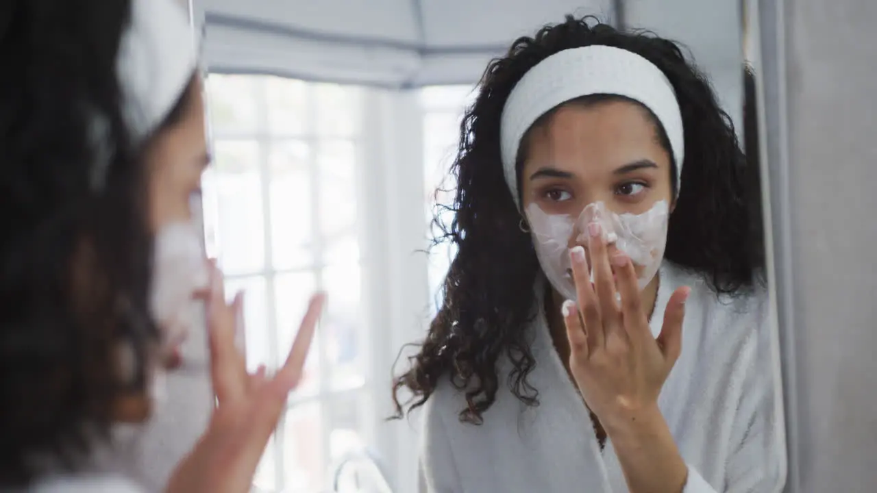 Mixed race woman applying face cream in bathroom