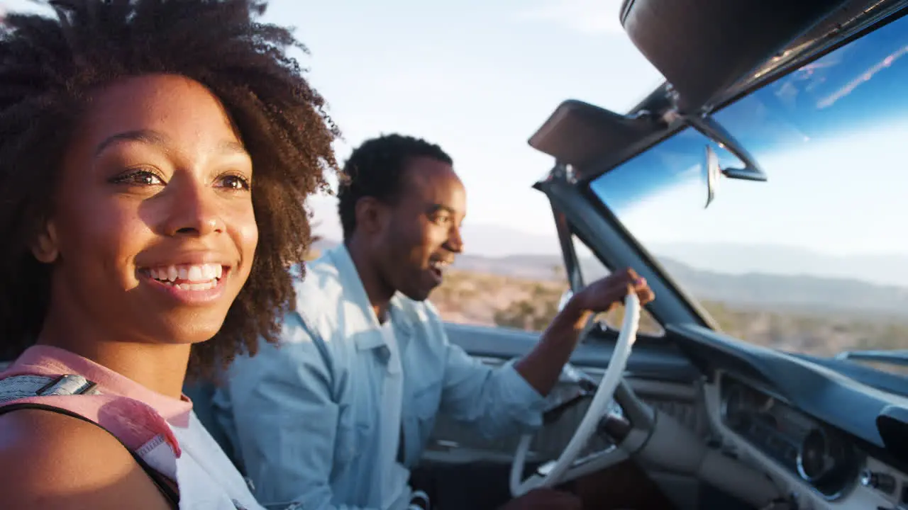 Young black couple driving in open car close up side view