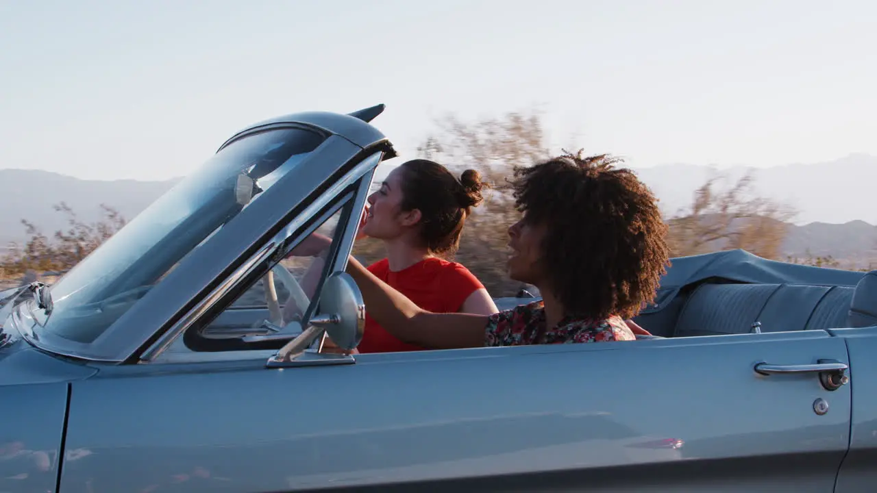 Two female friends pointing from a convertible car