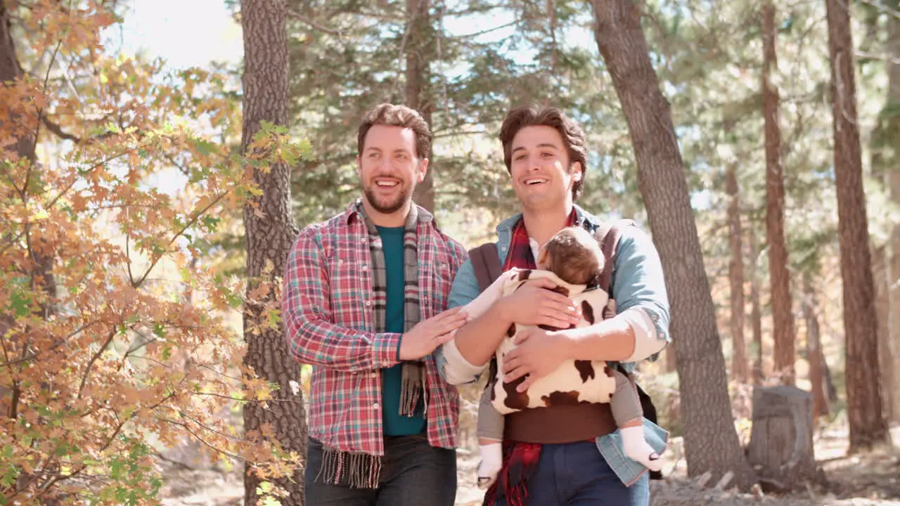 Male parents in forest with baby in sling pass out of shot