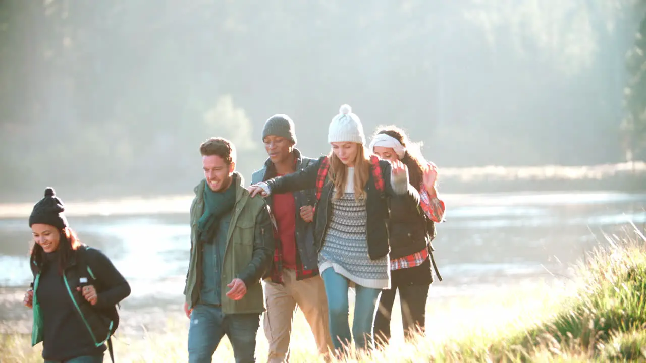 Five friends on a camping trip walking in a row near a lake