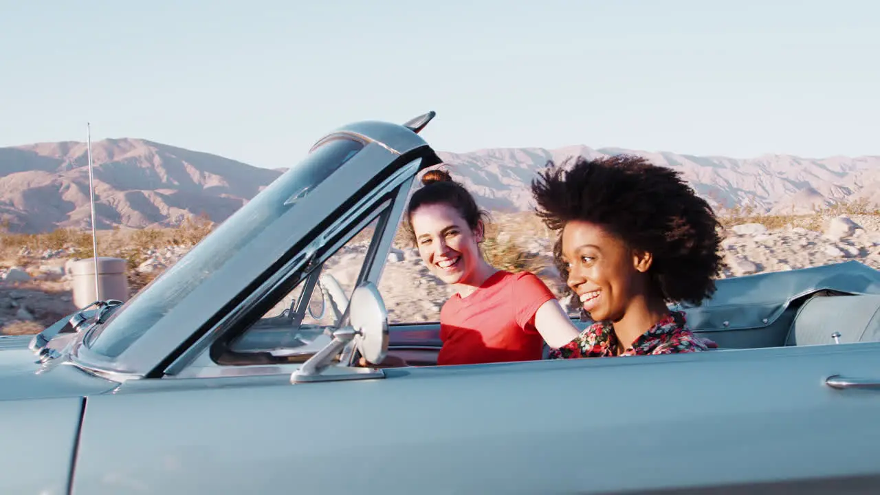 Two female friends driving an open car on a desert highway