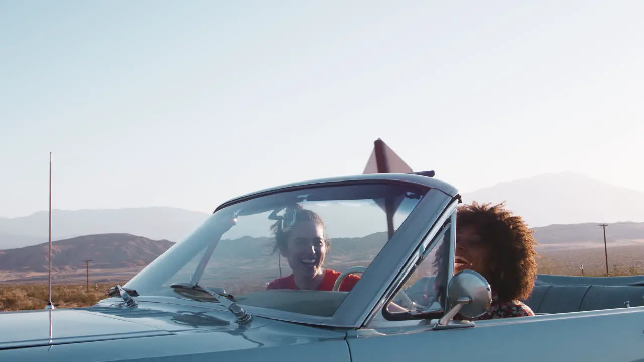 Laughing female friends driving in convertible on a highway