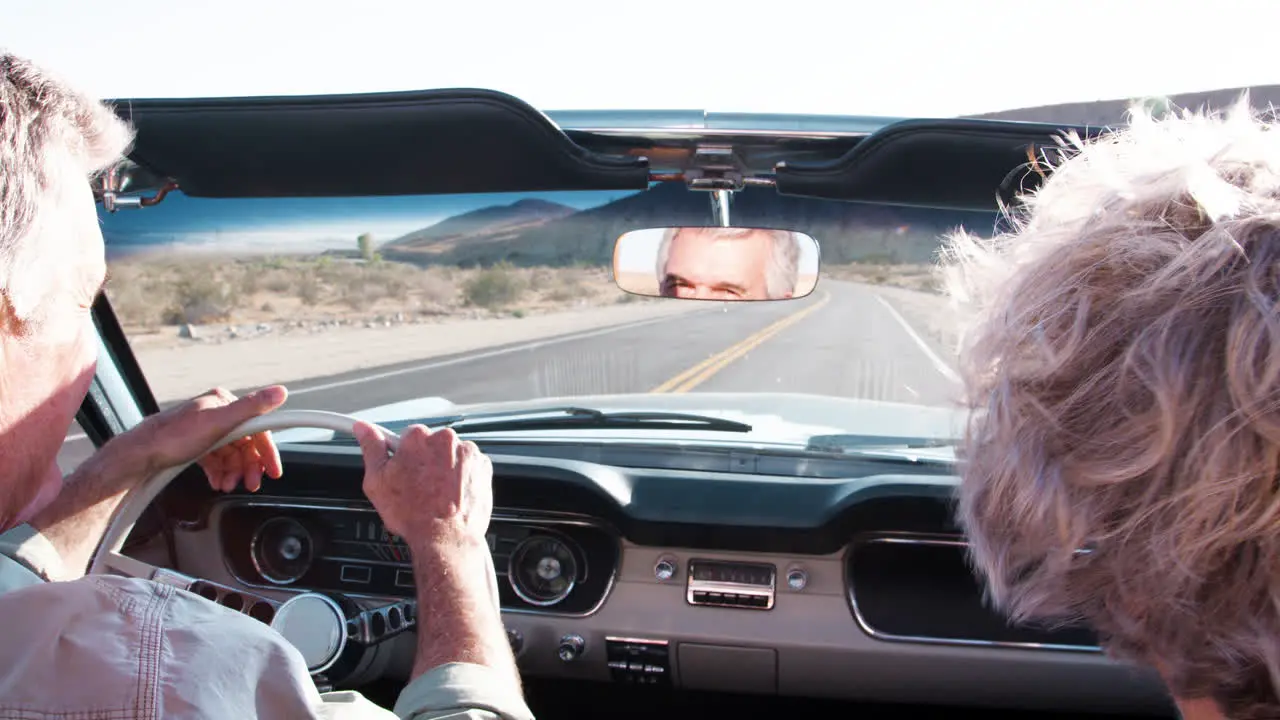 Senior couple driving old convertible back view close up