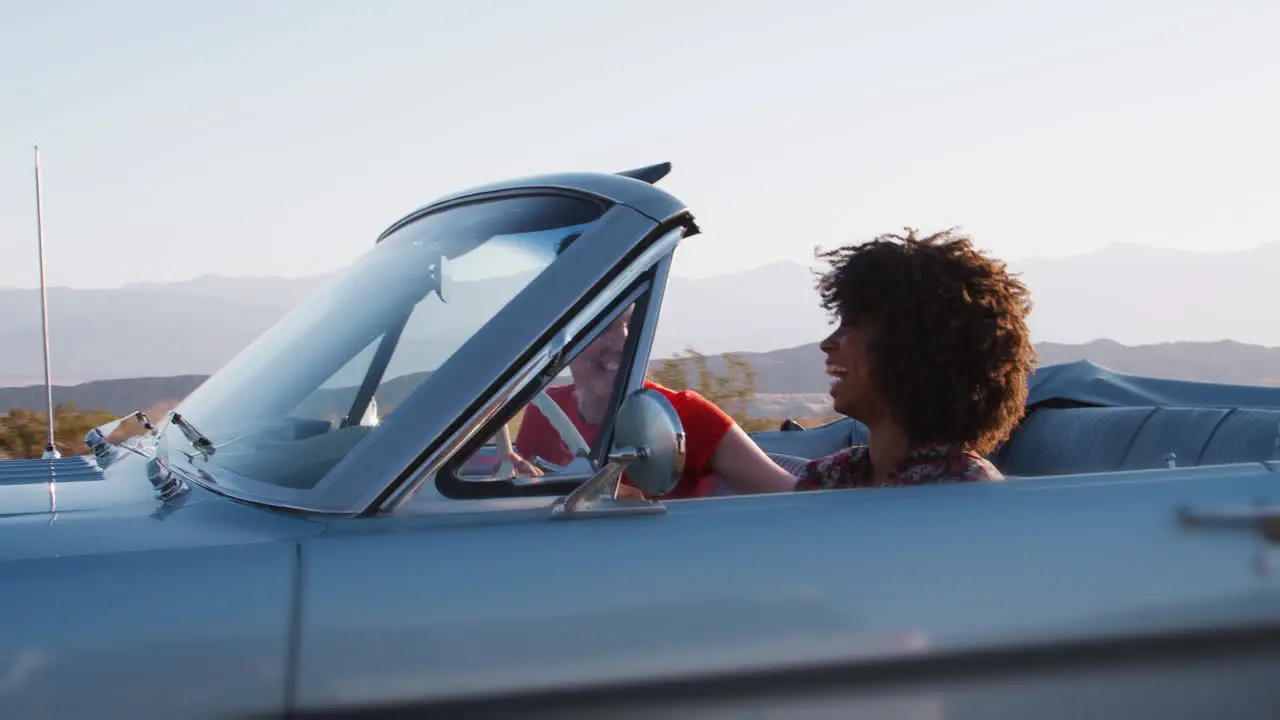 Happy female friends driving in convertible one raising arm