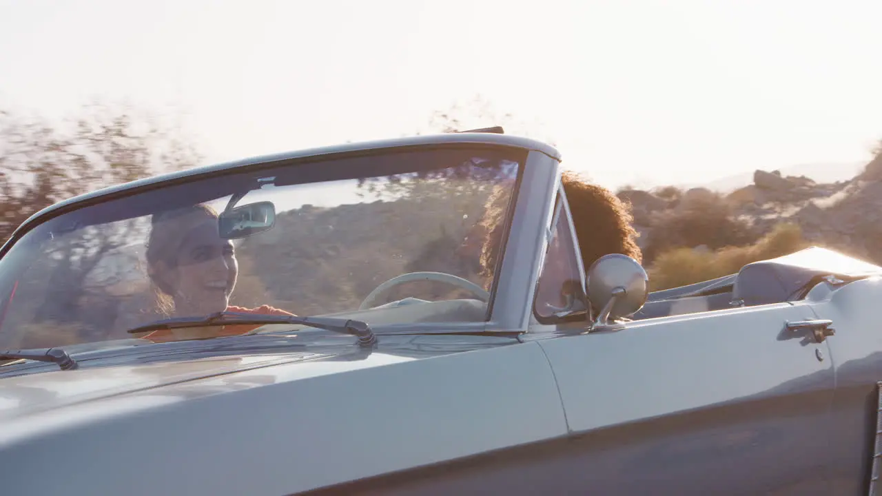 Laughing female friends in convertible on highway low angle