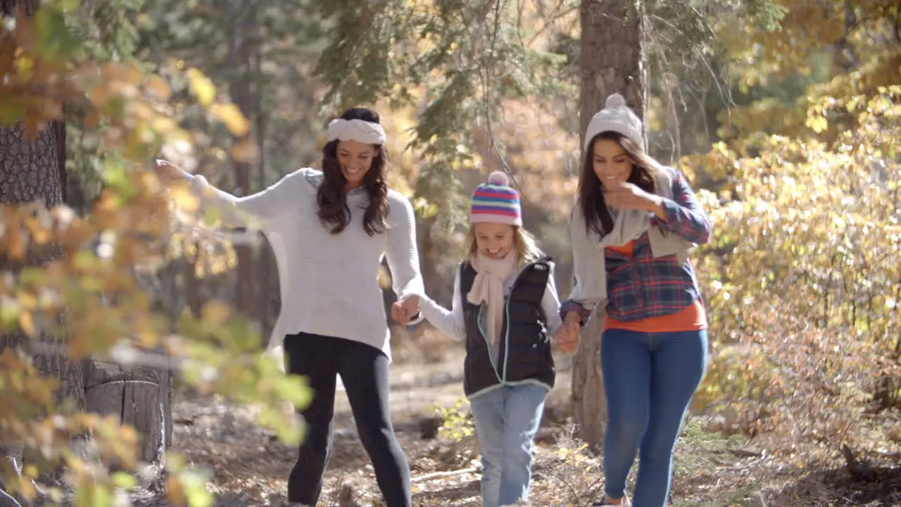 Female parents walk in a forest holding hands with daughter