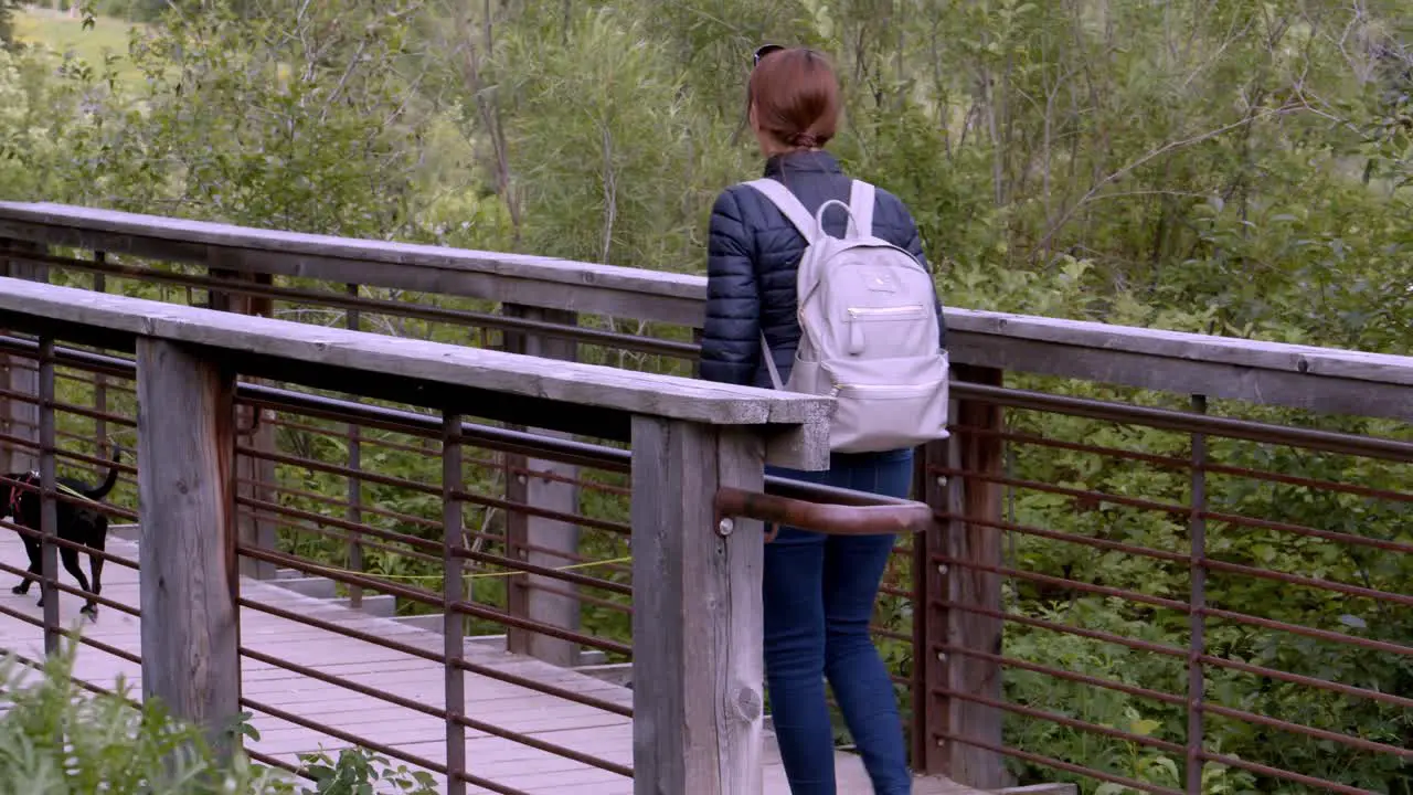 Woman walking small black dog over a narrow bridge