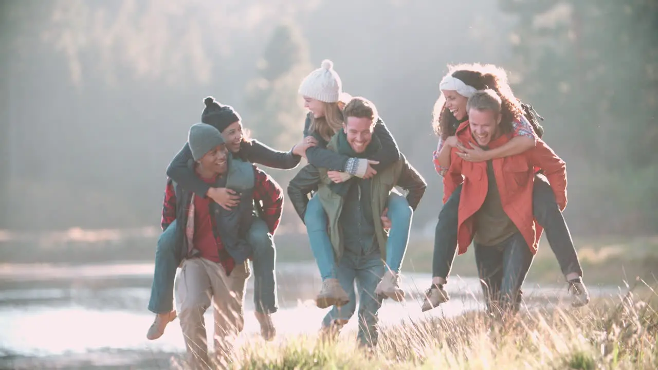 Six friends have fun piggybacking in the countryside by lake