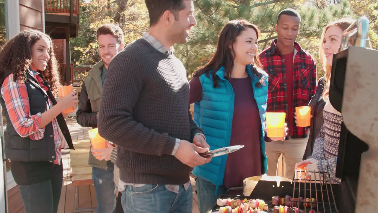 Friends stand talking at a barbecue one tends to the grill