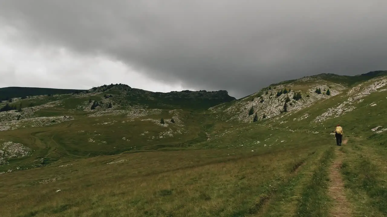 Pan wide angle shot revealing a hiker crossing a mountain alpine valley and some storm clouds