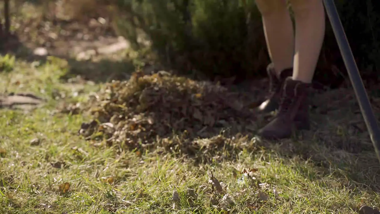 Close-up view of unrecognizable woman in boots removing weeds with a rake in the countryside