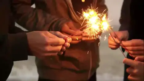 Close Up view of hands of group of people holding bengal lights and lightning them up on the beach during sunset