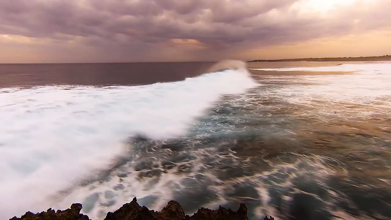 TimeLapse Waves rolling in during sunset with motion blur moody clouds in sky