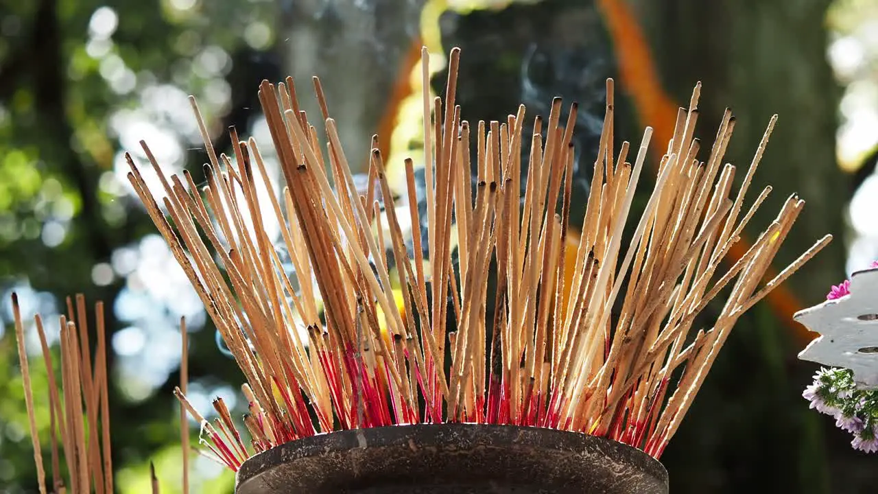 Burning incense sticks and smoke in sunlight with lip of pot