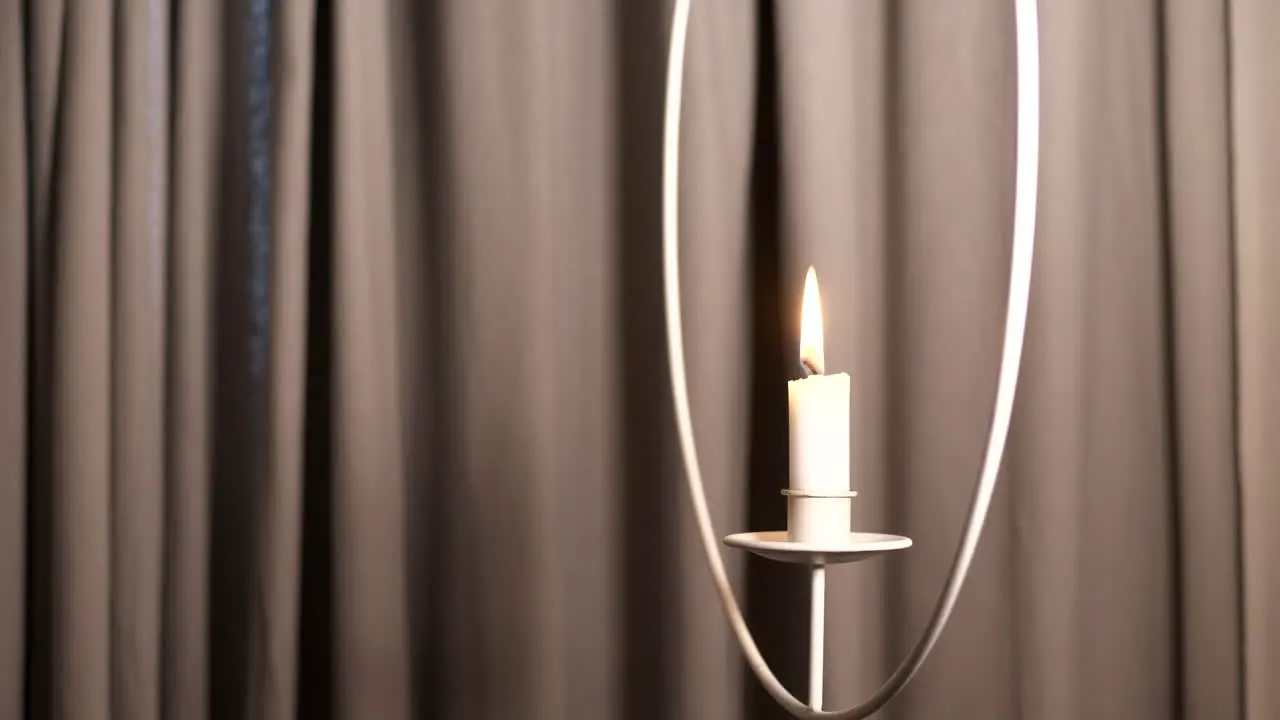 Beautiful shot of burning hanging candle against plain coloured background curtain