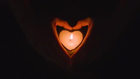 Romantic Lit Heart Shaped White Candle On Black Background Being Held By Hands