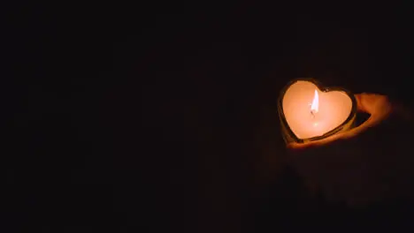 Hand Putting Romantic Lit Heart Shaped White Candle Onto Black Background