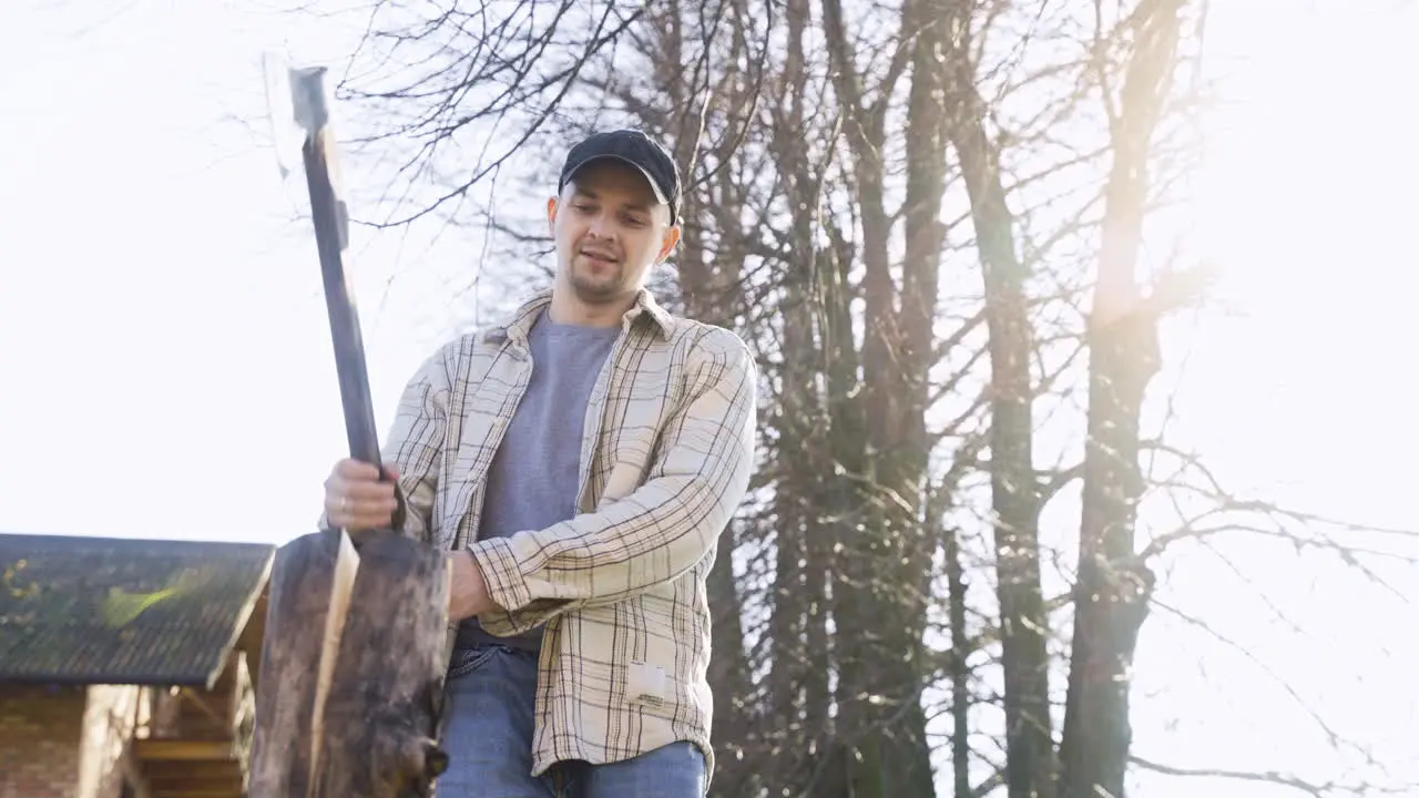 Bottom view of caucasian man chopping firewood with an ax outside a country house