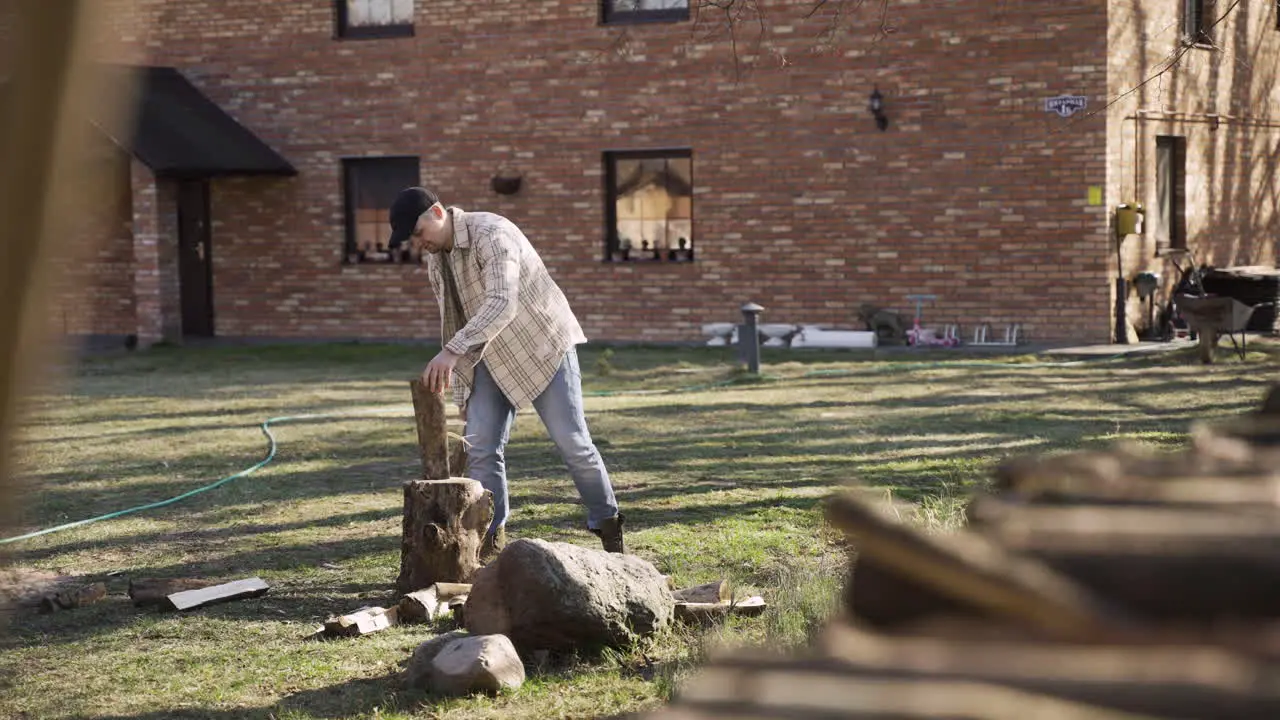 Distant view of caucasian man chopping firewood with an ax outside a country house