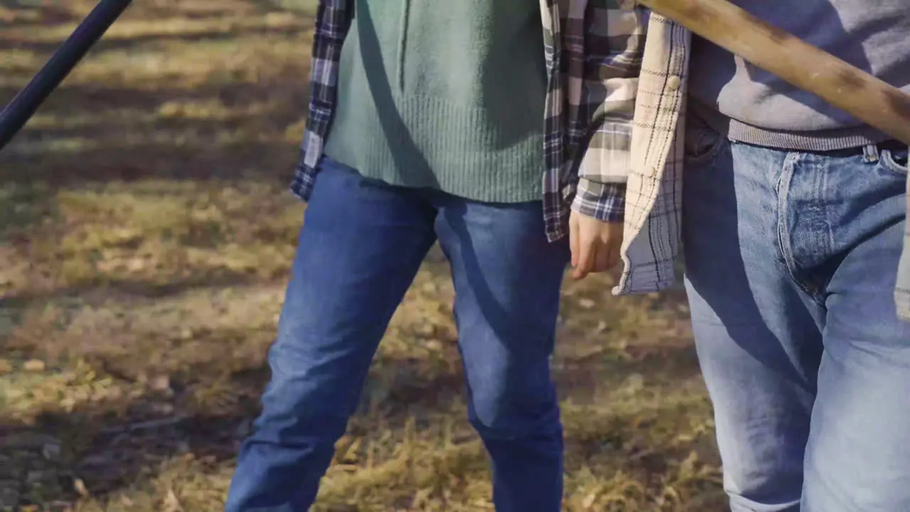 Close-up view of unrecognizable couple carrying rakes while walking throught the countryside