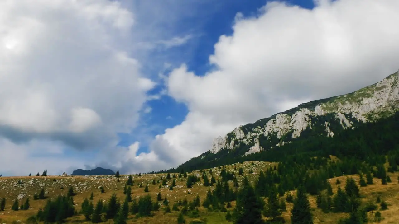 Timelapse of clouds passing over a meadow a pine forest and a mountain cliff