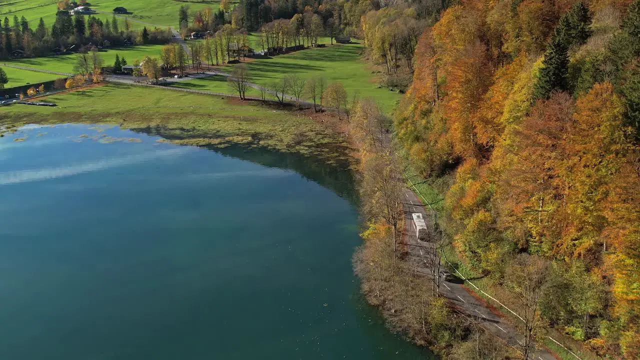 Aerial View Over Autumnal Forest Trees Beside Lake And Road Surrounding It