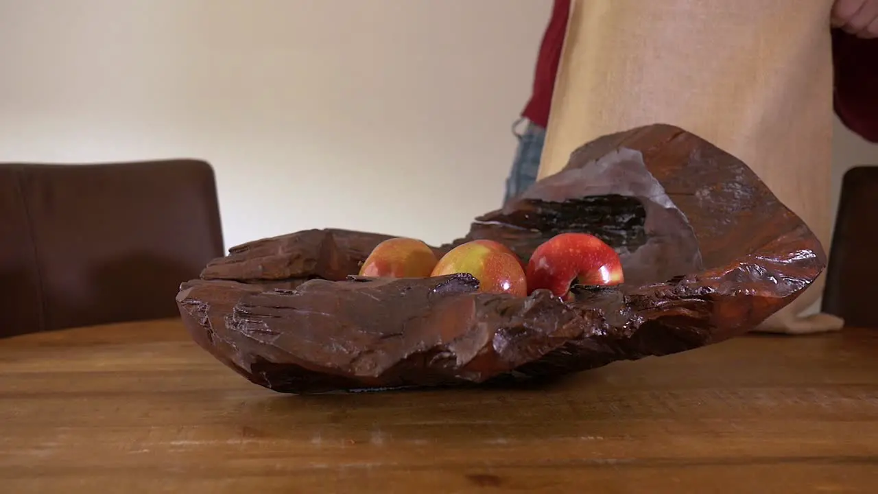 Male hands take fruits from a bag and put them in a wooden bowl standing on a wooden table panning shot