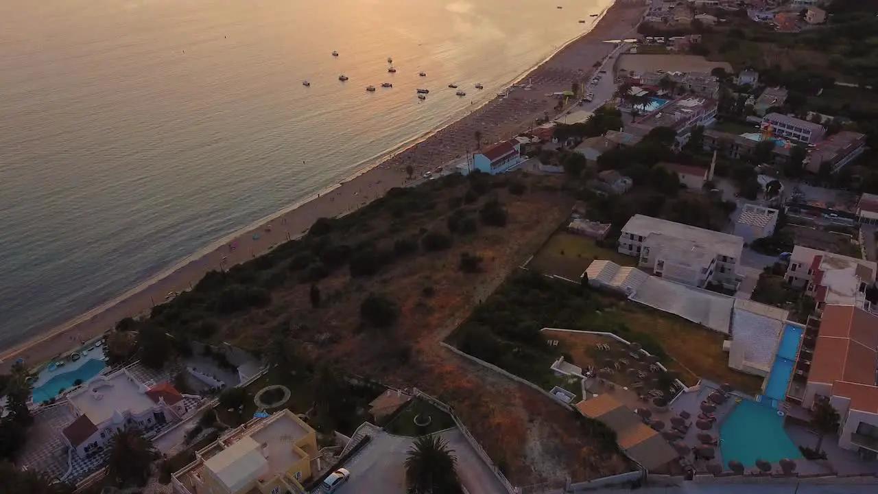 Aerial shot of orange sunset beach full od umbrellas hotels and small floating boats in Greece