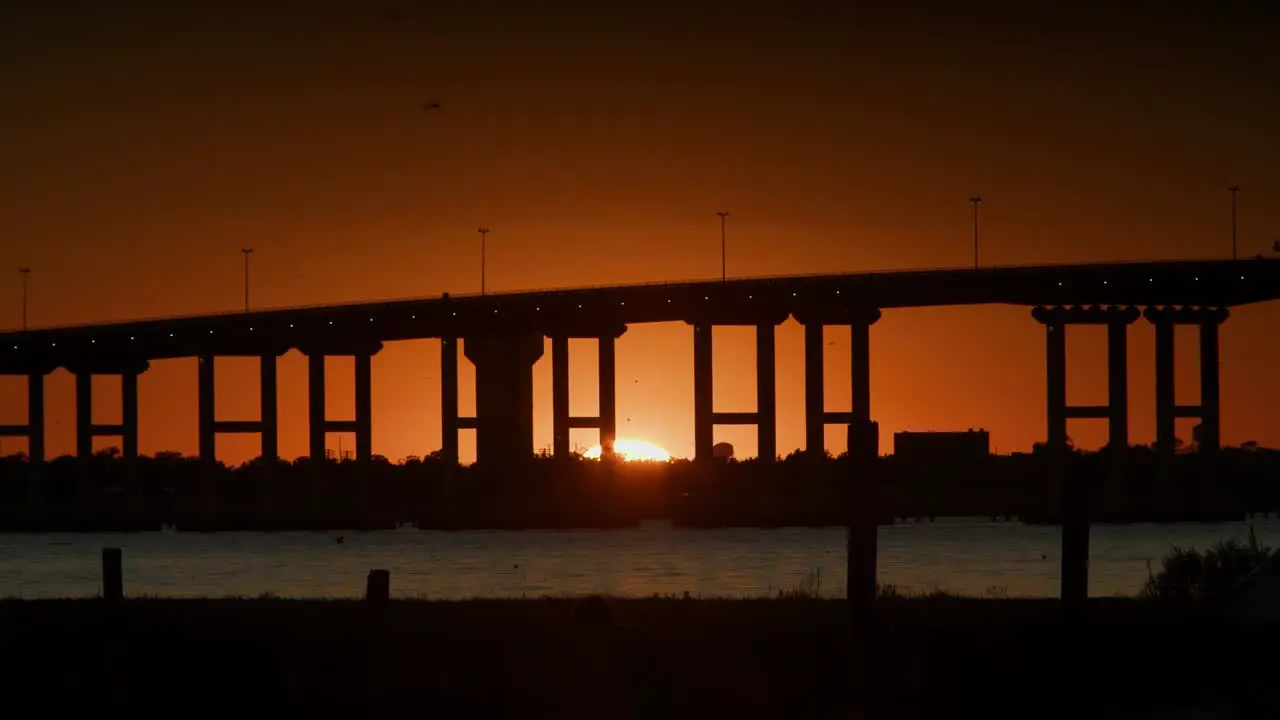 A beautiful sunset under a bridge over water while people walk through the foreground